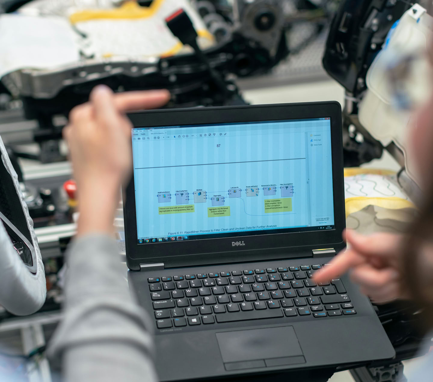 Engineers using a laptop to analyze software data in an industrial workshop setting.